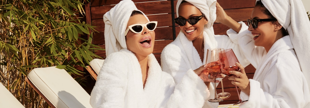 Three women in bathrobes, sunglasses and towels on their heads.